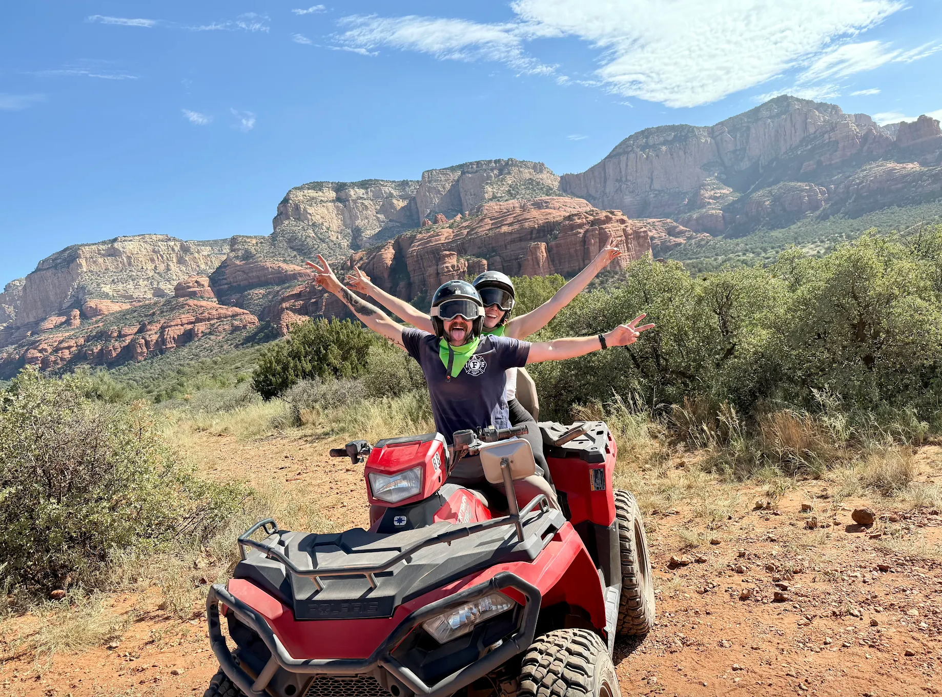 Two happy customers on their red ATV with red rocks in the background.