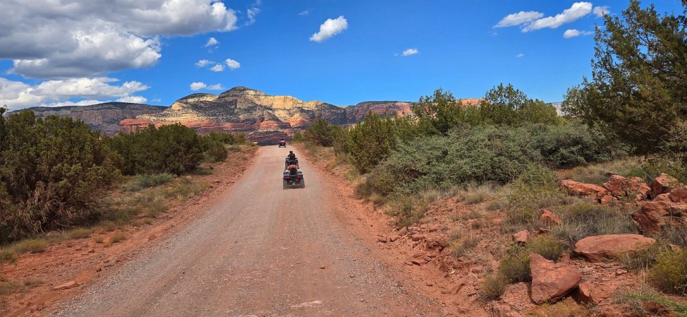 Vibrant orange and red rock formations, lush greenery, and winding trails under a clear blue sky, showcasing an adventurous ATV navigating through Sedona's hidden canyons and scenic viewpoints, capturing the essence of exploration and nature’s beauty.