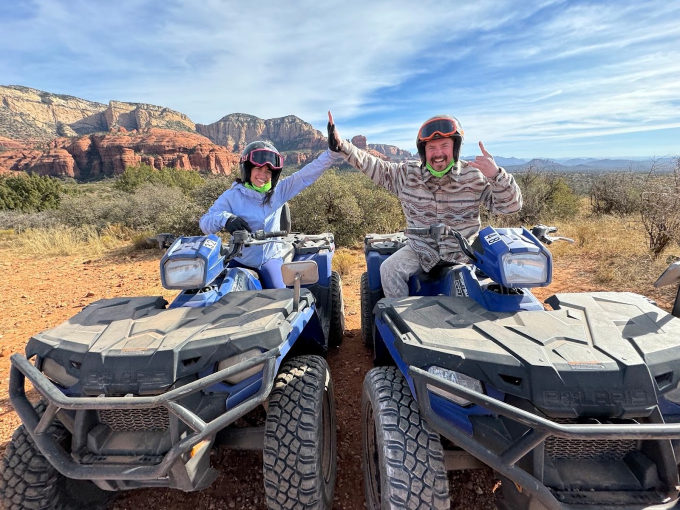 A breathtaking view of Sedona's red rock formations with an ATV parked on a rugged trail, surrounded by vibrant desert flora, under a clear blue sky, showcasing the thrill of off-road adventure and natural beauty.